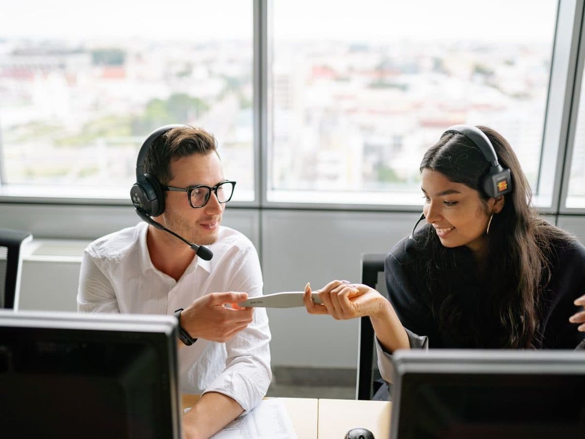 Dois atendentes com headset conversam em escritório com vista da cidade